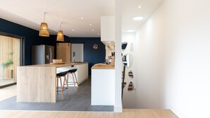 Une cuisine moderne dotée d’un îlot central, de tabourets en bois et de luminaires suspendus.