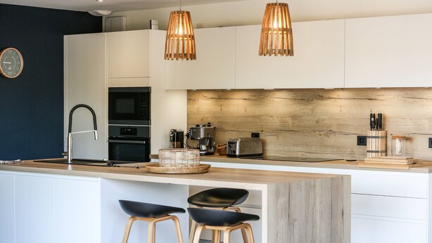 Une cuisine moderne dotée d’un îlot central, de deux tabourets de bar, d’un éclairage suspendu et d’un pare-feu en bois.