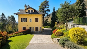 A yellow building with a stone pathway leading to the entrance, surrounded by well-maintained gardens and trees. - Villa Rosa - villa surrounded by greenery with private garden, ideal for families (Pian Nava)