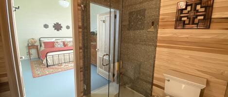 A bathroom with a glass shower enclosure, a toilet, and a wooden wall.