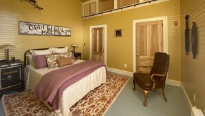 Une chambre à coucher avec un lit, une chaise, une table de chevet, une lampe, un tapis et un tableau accroché au mur.