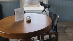 Une table ronde en bois, sur laquelle est posé un présentoir à menus, un télescope sur un trépied et une chaise.