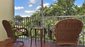 A balcony with wicker furniture, a glass table, and a view of trees and sky.