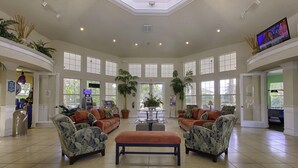 A spacious lobby with a high ceiling, large windows, and a central seating area with sofas and a coffee table.
