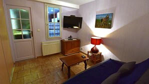 Un petit salon avec un canapé, une table en bois, un téléviseur, un meuble et une fenêtre avec des rideaux.