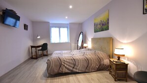 Une chambre à coucher comprenant un lit, un bureau, une chaise, une télévision, une fenêtre et des œuvres d’art.