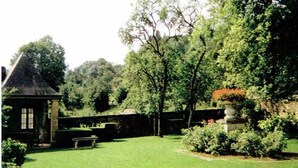 Un jardin agrémenté d’un bâtiment en pierre, d’un banc et de divers arbres.