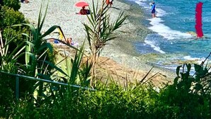 Une plage de galets avec une eau d’un bleu limpide, des palmiers et quelques personnes qui profitent du soleil.