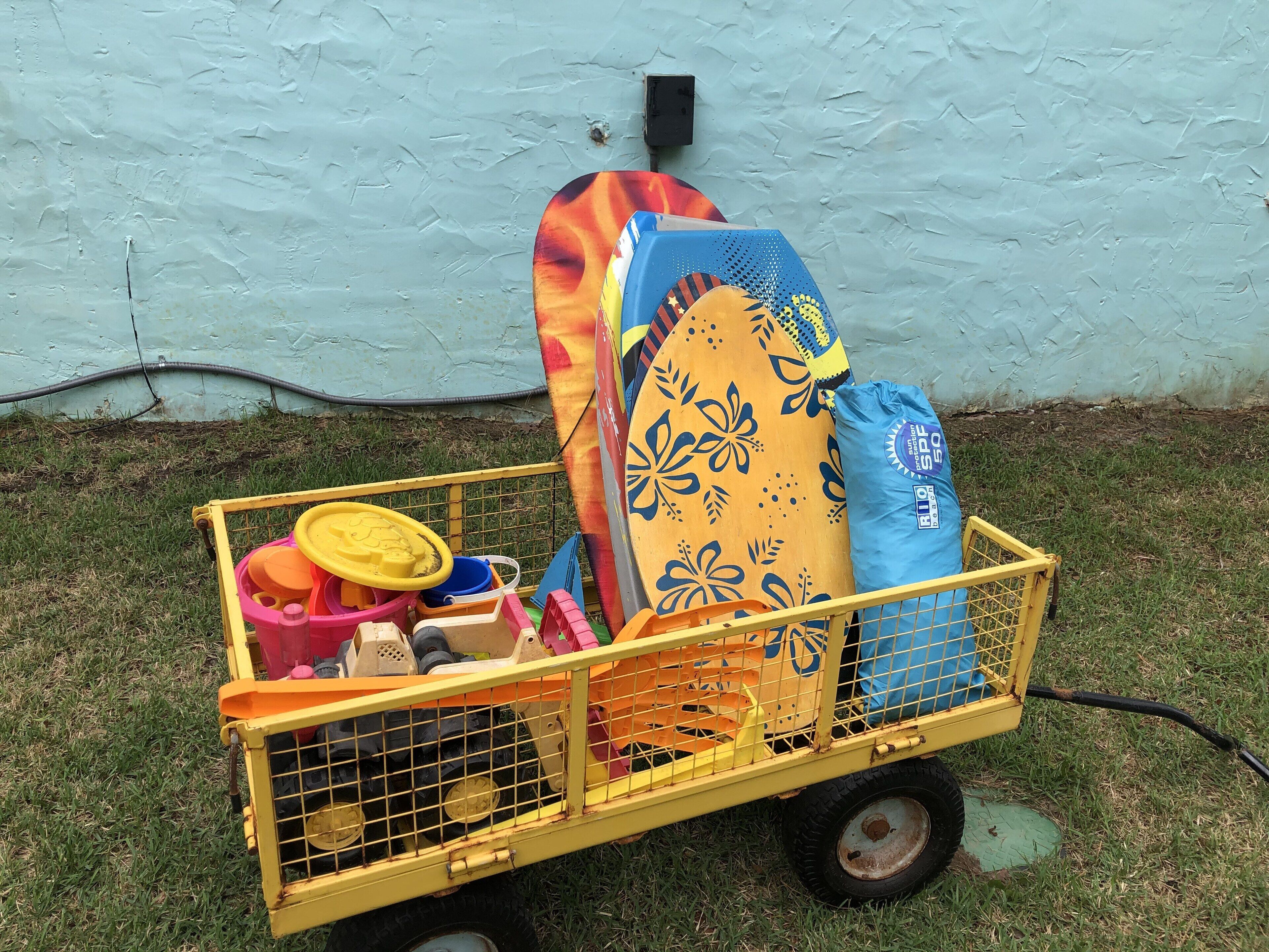 Un carro amarillo con una tabla de surf, una bolsa azul y varios recipientes de colores.