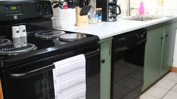 Een keuken met een zwarte kookplaat, een koffiezetapparaat en een afwasservoordeel.