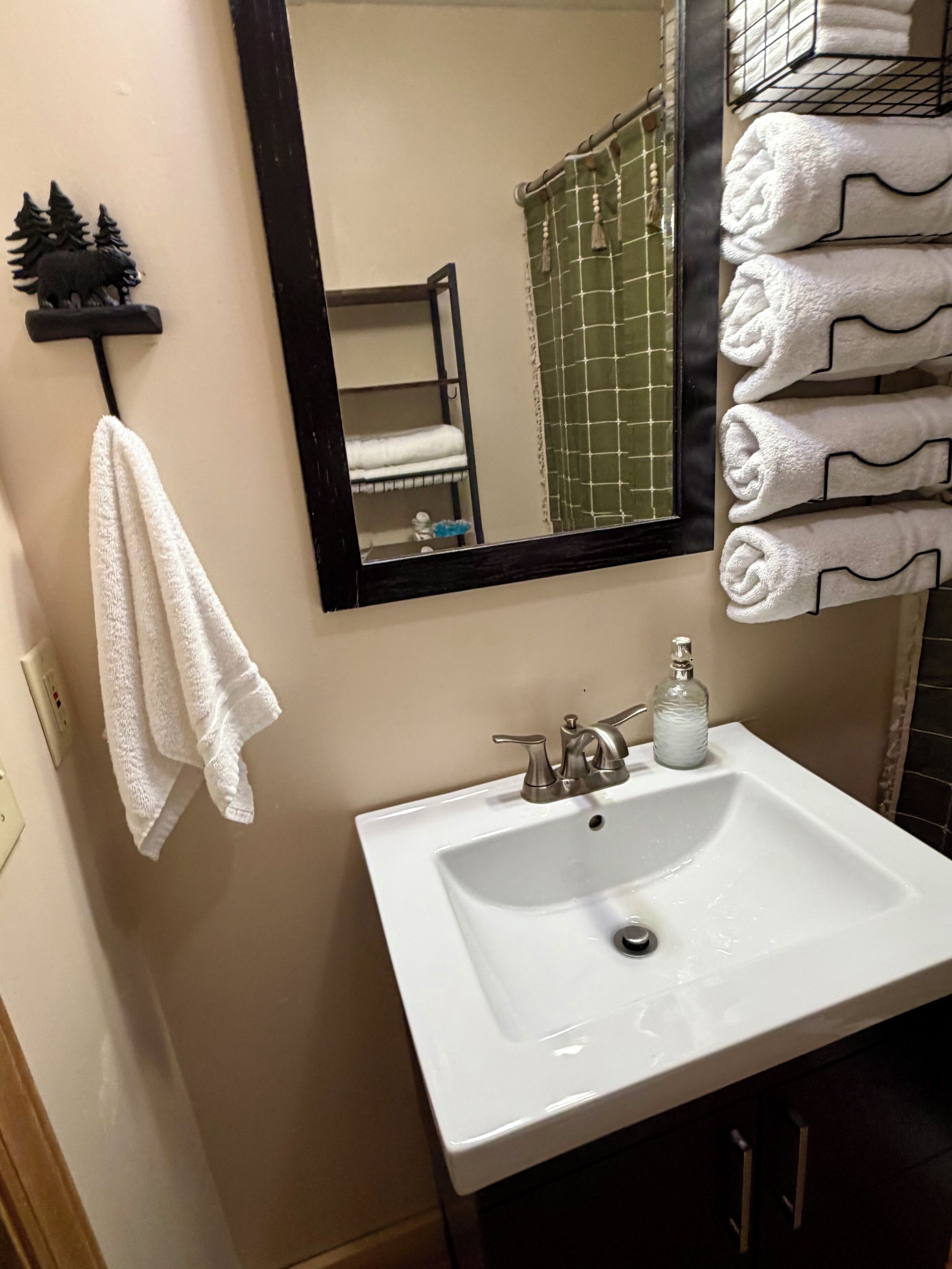 A bathroom with a white sink, a mirror, a towel rack with towels, and a small shelf with a decorative item.