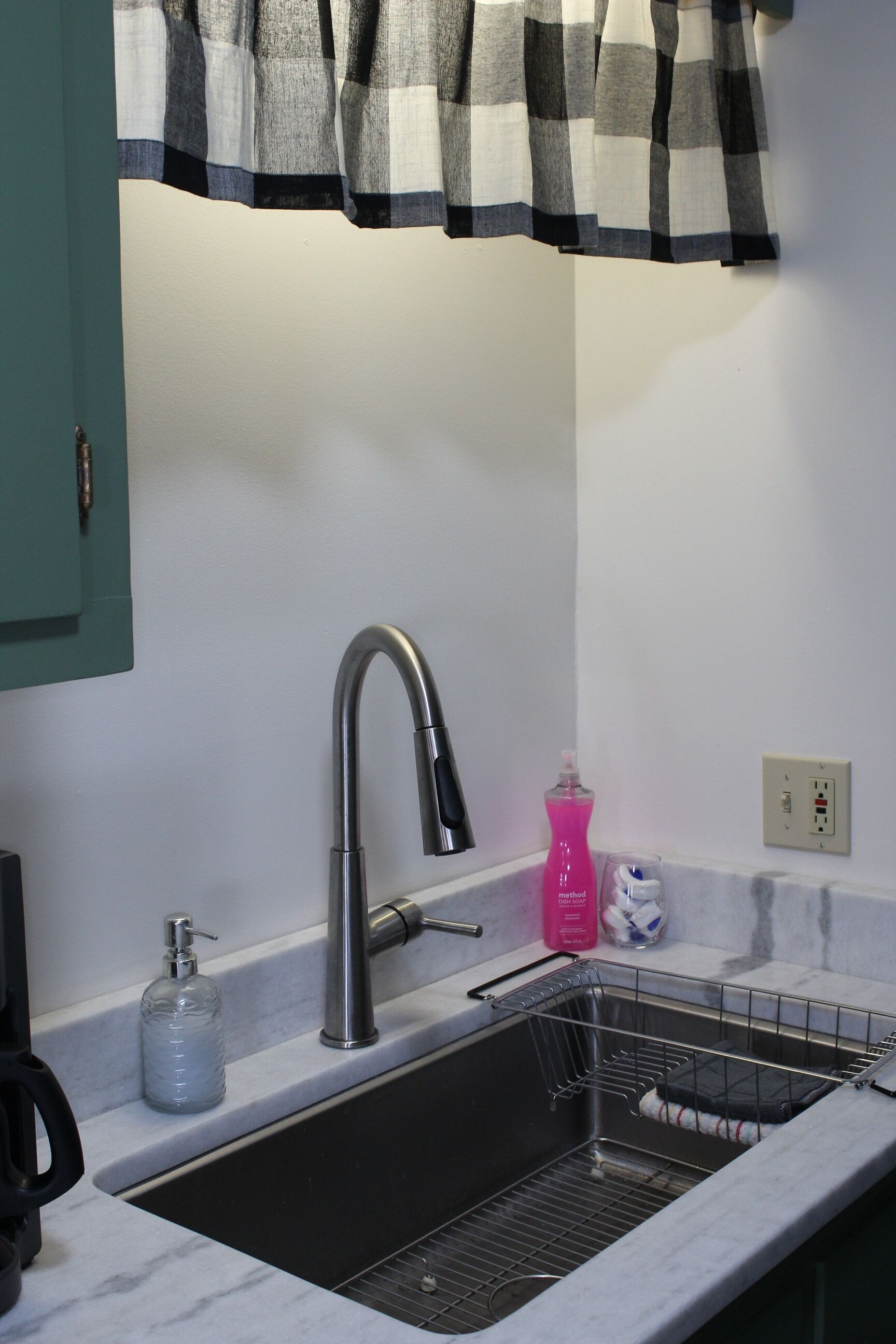 A kitchen with a stainless steel sink, a faucet, a soap dispenser, and a dish rack.