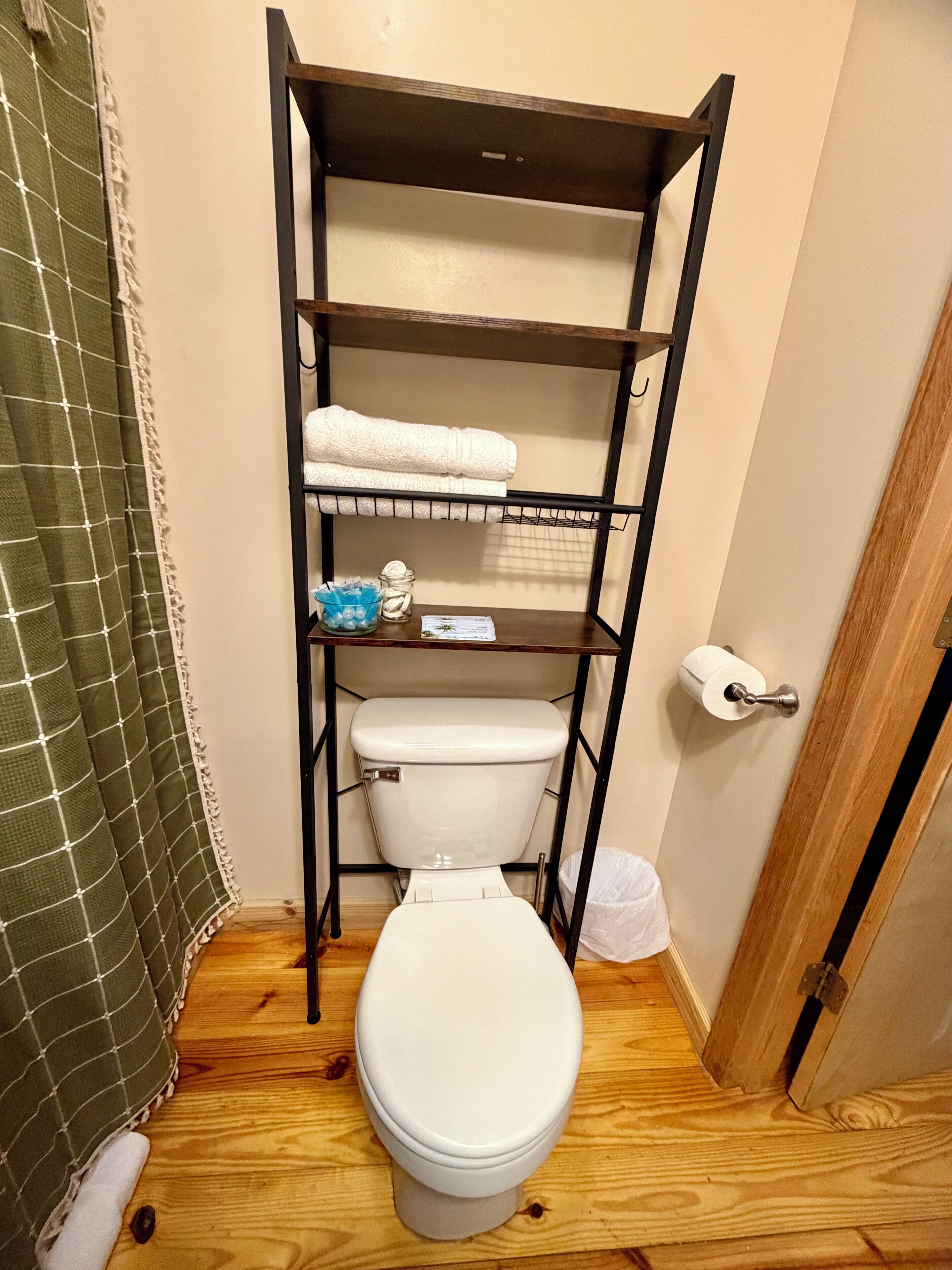 Een kleine badkamer met een wit toilet, een plankje met een handdoek en toiletartikelen, en een douchegordijn.