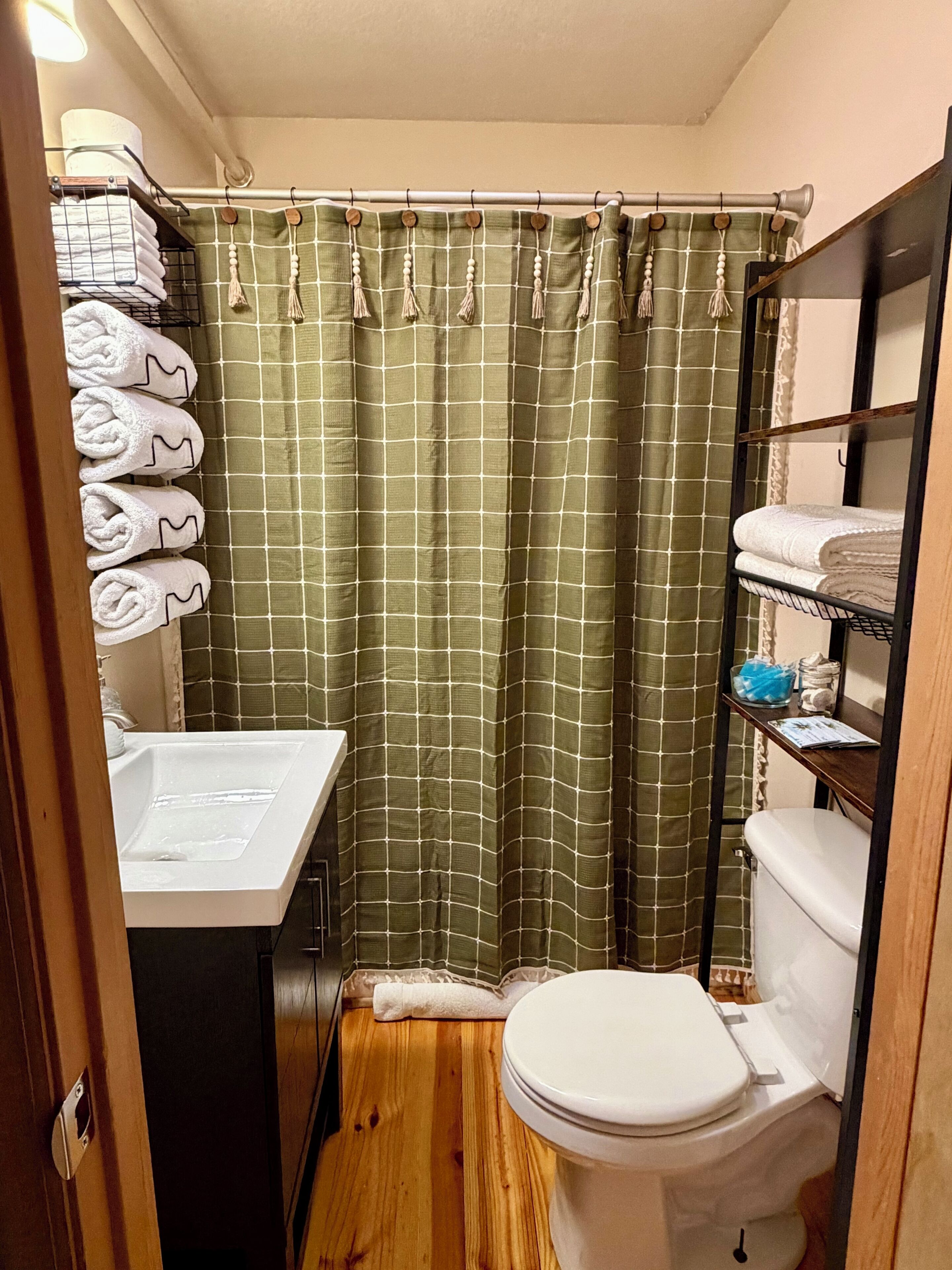 A compact bathroom with a shower curtain, a toilet, a sink, and shelves with towels.