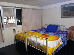 Ein Schlafzimmer mit einem Bett, einem Fenster mit Vorhängen, einem Bild an der Wand und einem Metallbettgestell.