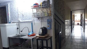 A kitchen with a sink, a kettle, and a shelf with dishes.
