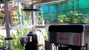 A coffee machine with a menu, a glass container, and a window view of greenery.