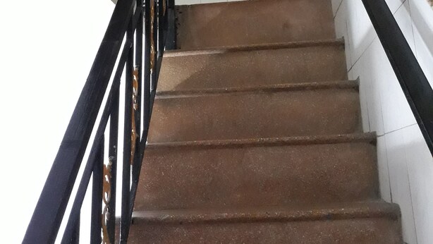 A staircase with a handrail, tiled walls, and a painting of a house.