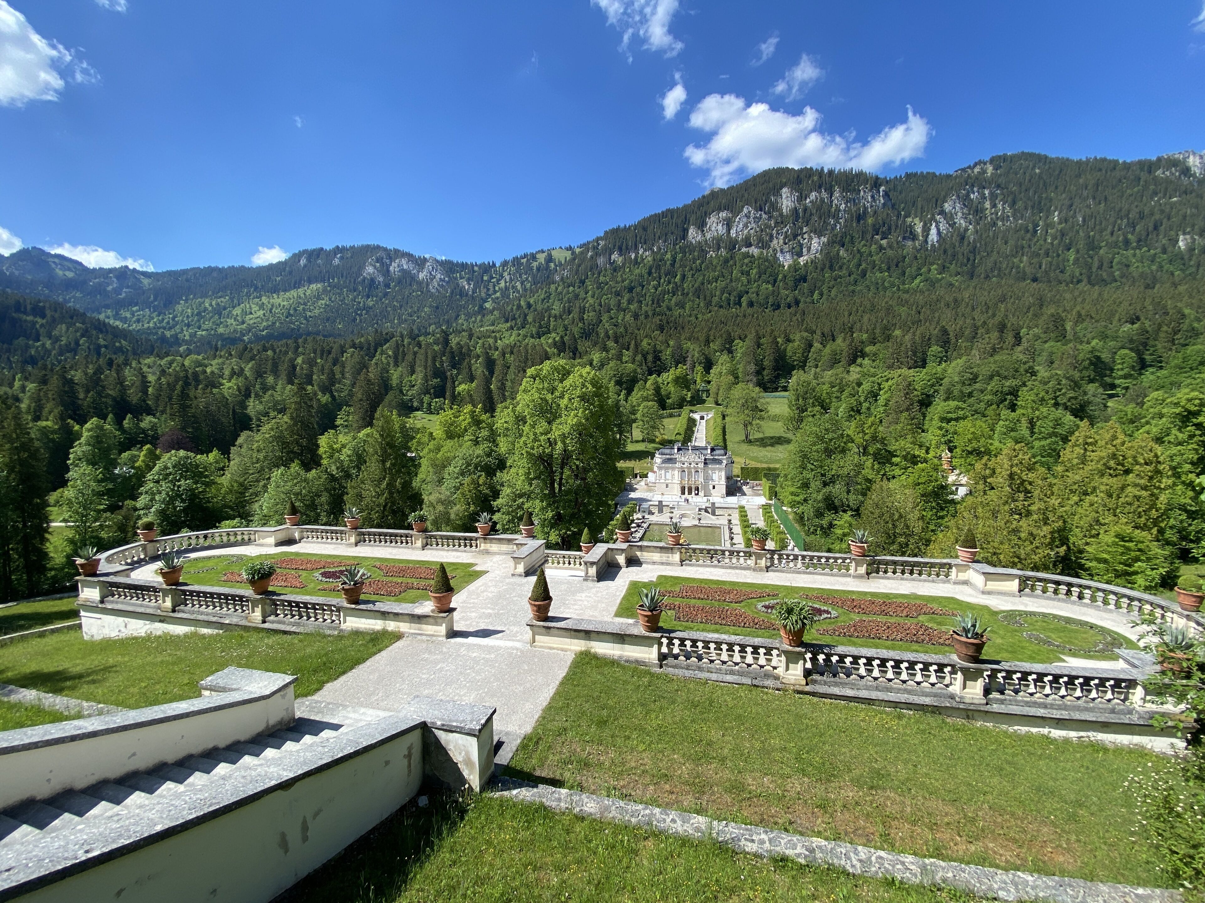 A grand estate with a symmetrical garden, a central fountain, and a mountain backdrop.
