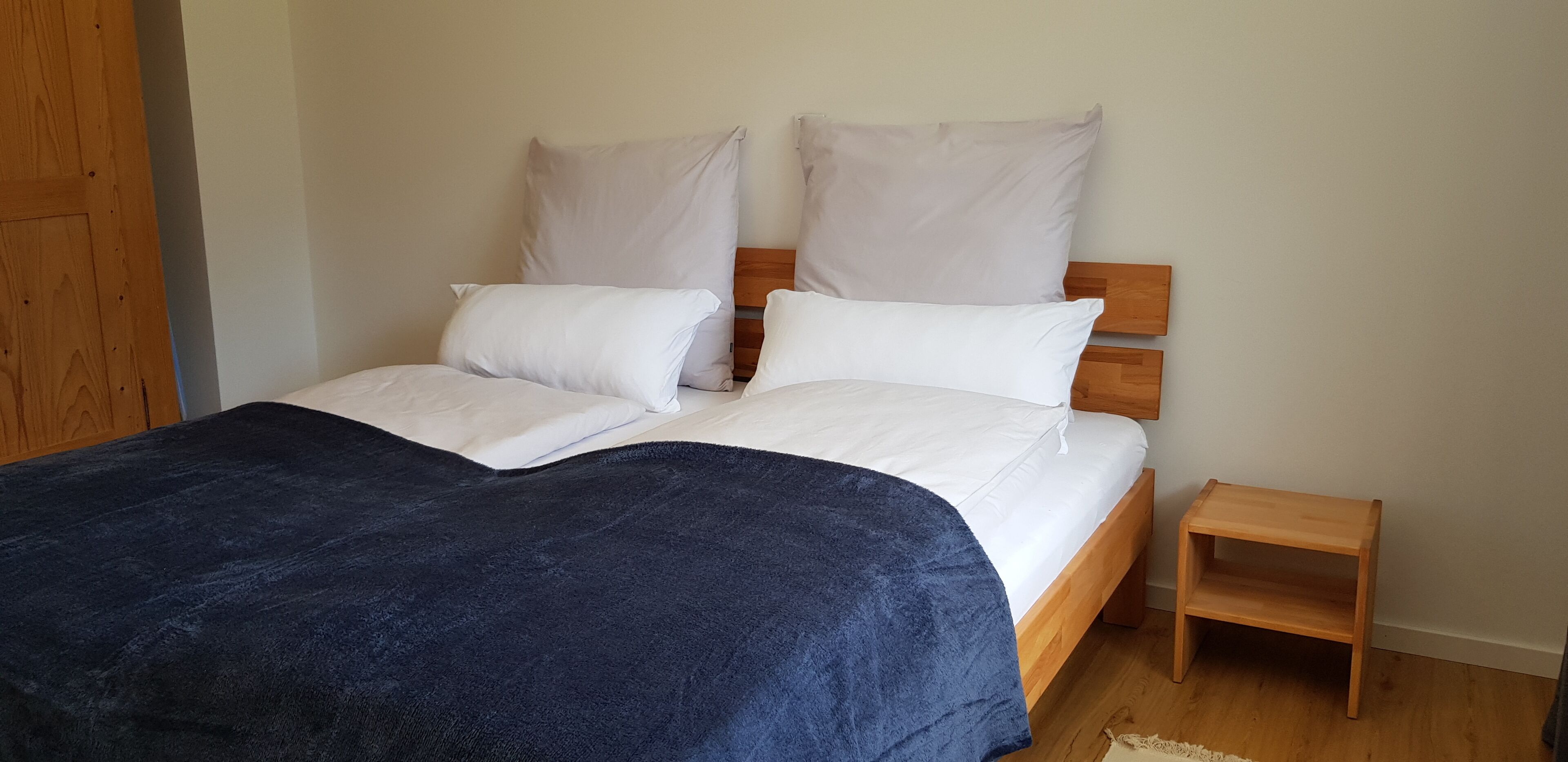 A bed with white bedding and a blue blanket, a wooden bedside table, and a wooden headboard.