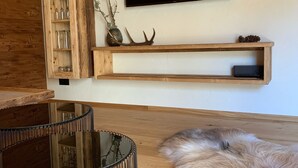 A modern living room with a wooden TV stand, a mounted TV, a glass table, and a fluffy rug.