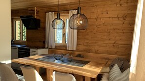 A wooden interior with a dining table, chairs, and pendant lights.