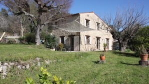 Una casa de piedra con techo de tejas, rodeada por un patio cubierto de césped y plantas en macetas.
