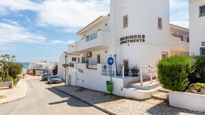 A white building with "MARINERS APARTMENTS" signage, a cobblestone street, parked cars, and potted plants. - Mariners (1) - Bright and stylish apartment - walk to the beach (Luz)