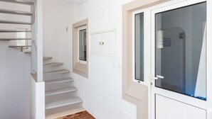 A staircase with a handrail, a door with a window, and a wall-mounted light fixture. - Mariners (1) - Bright and stylish apartment - walk to the beach (Luz)