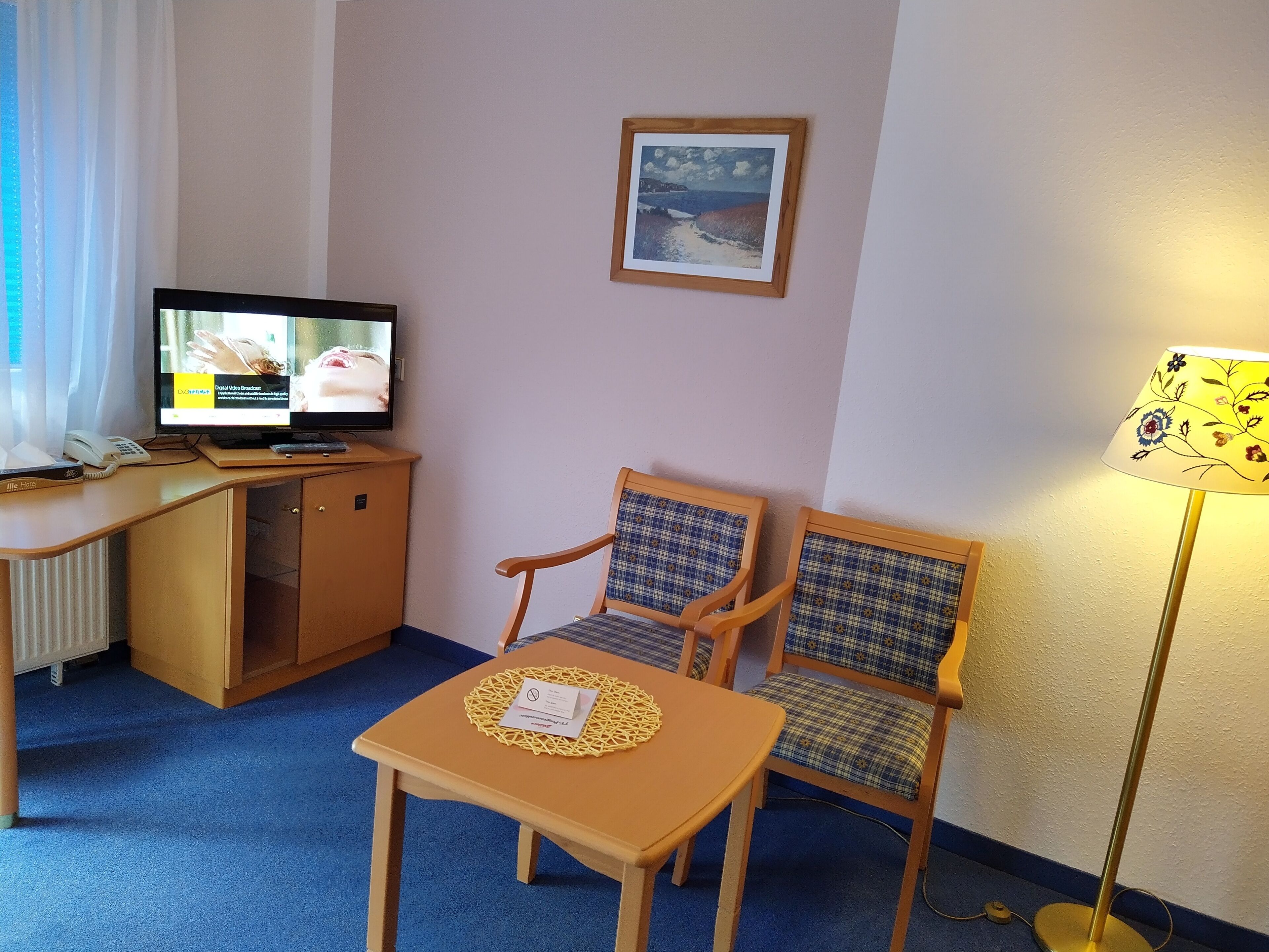 Ein Hotelzimmer mit Schreibtisch, zwei Stühlen, Fernseher und Lampe.