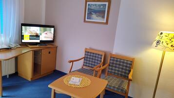 Ein Hotelzimmer mit Schreibtisch, zwei Stühlen, Fernseher und Lampe.