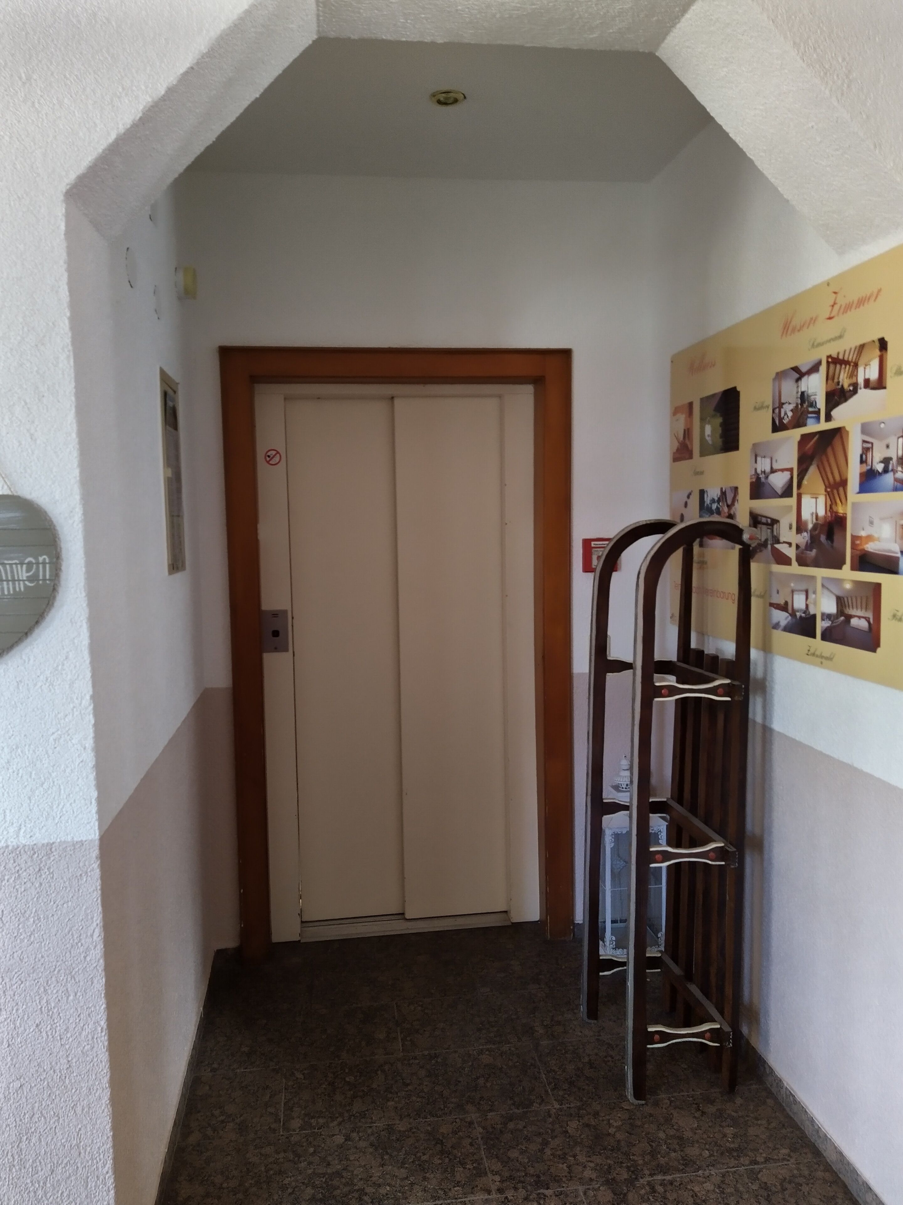 Un couloir avec une porte fermée, un porte-objets fixé au mur et un tableau d’affichage où sont accrochées des photos.