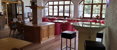 A spacious restaurant with wooden flooring, red seating, and large windows offering views of the outdoors.