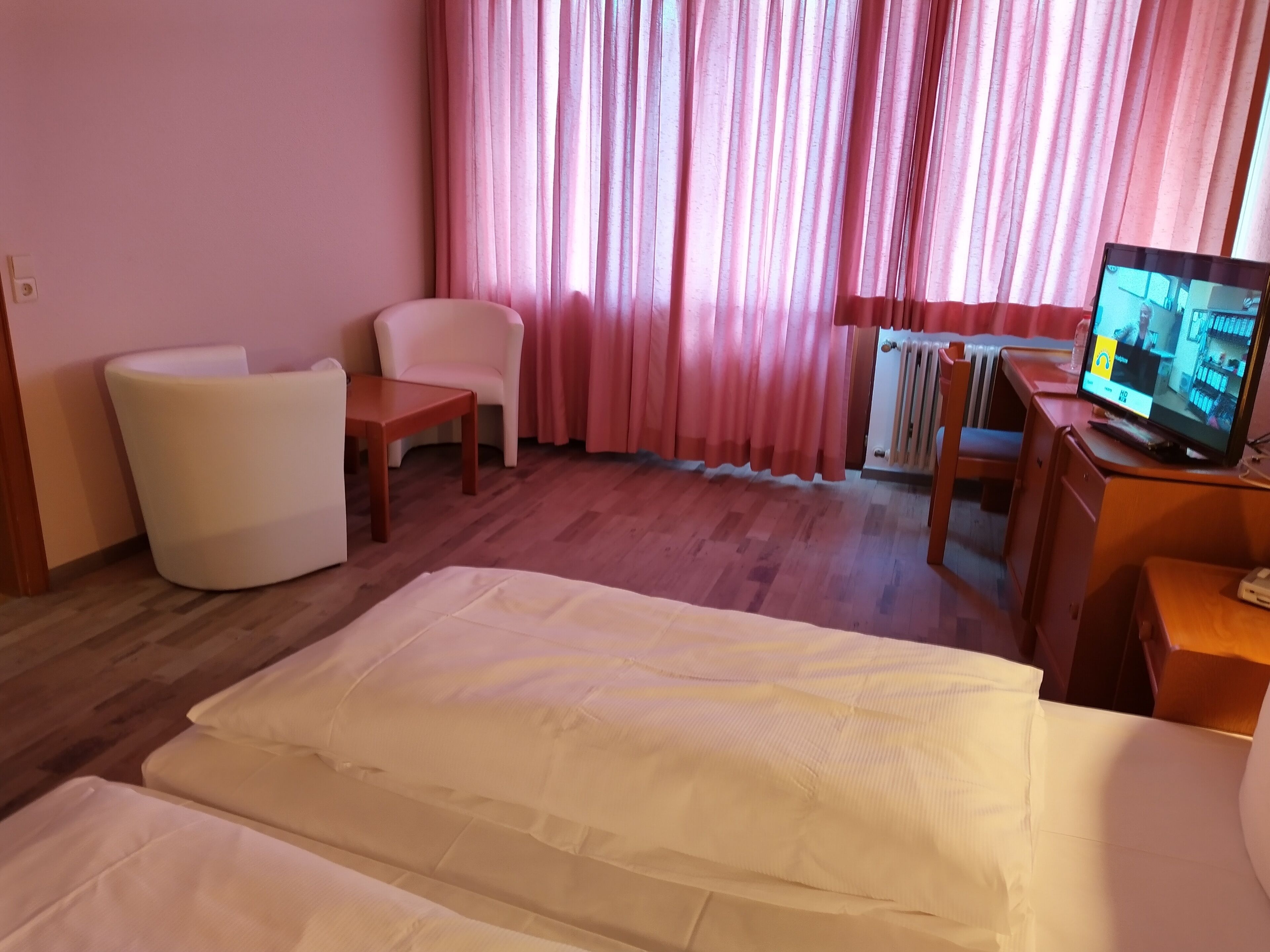 A hotel room with a bed, a desk, a chair, and a television.
