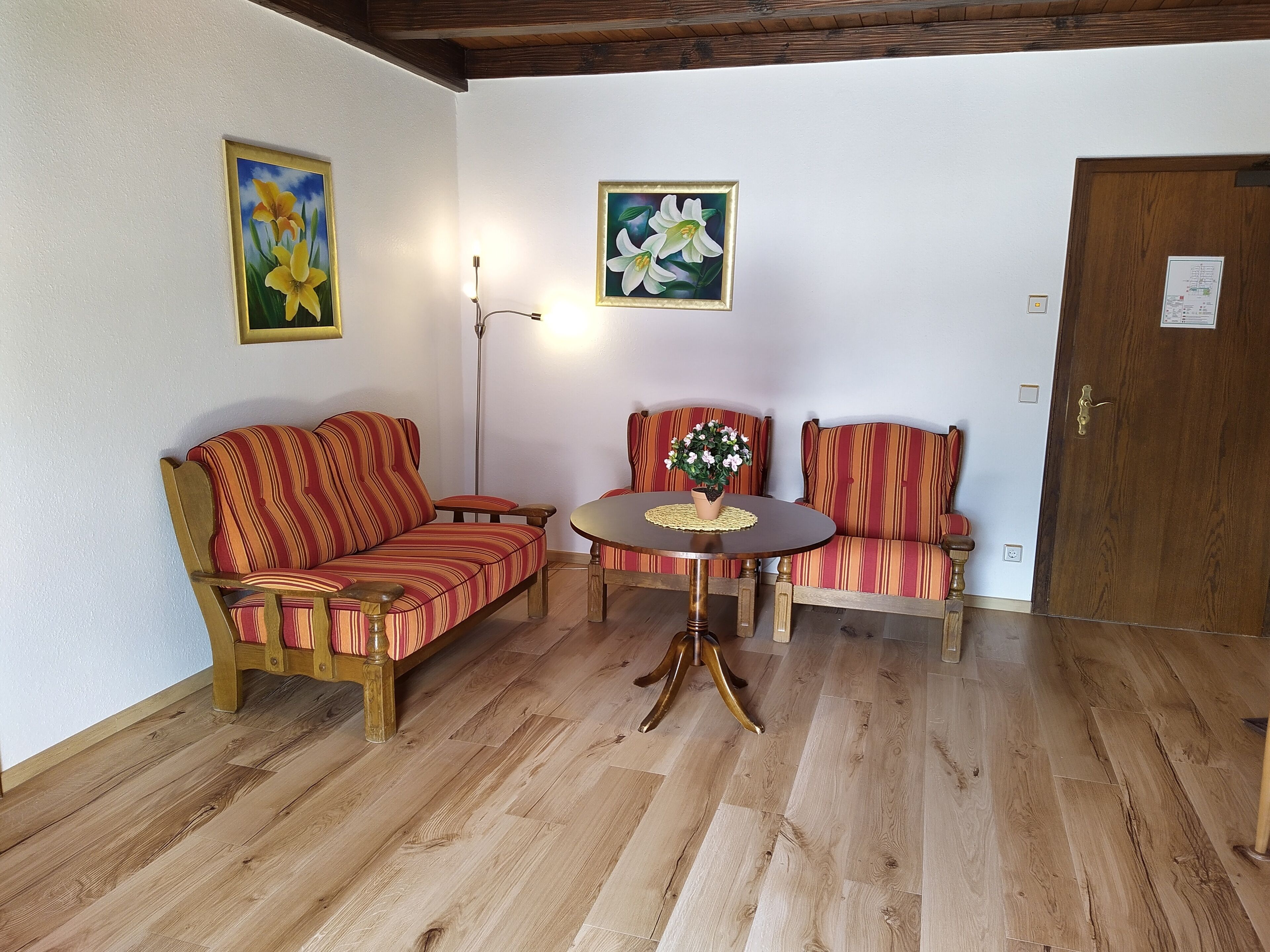 Une pièce avec un plancher en bois, un canapé, une chaise, une petite table et deux tableaux accrochés au mur.