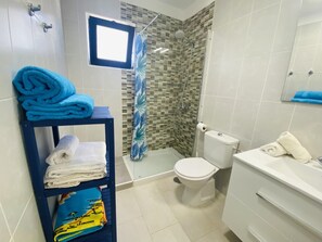 Une salle de bain avec une douche, des toilettes et un lavabo. Des serviettes sont posées sur un porte-serviettes et il y a une fenêtre au-dessus de la douche.