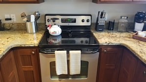 Une cuisine équipée d’une cuisinière, d’un four et de divers ustensiles. Des torchons sont accrochés à la poignée du four.
