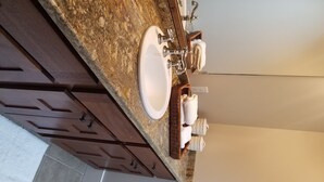Une salle de bain avec un comptoir en granit, un lavabo blanc et un meuble-lavabo en bois.