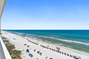 Ein Strand mit mehreren Reihen von Sonnenschirmen und Liegestühlen, ein sandiger Uferstreifen und das Meer.