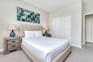 A bedroom with a large bed, two bedside tables with lamps, a wall art piece, and a closet.
