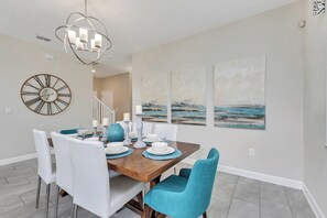 A dining area with a wooden table set for four, white chairs, and a large wall clock.