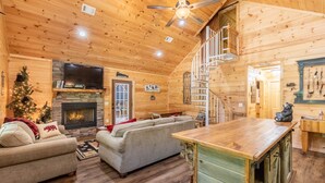 Un intérieur chaleureux de chalet en bois, avec une cheminée, un téléviseur, un escalier et un coin repas.