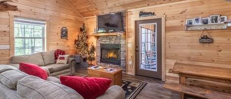 L’intérieur d’un chalet chaleureux, avec une cheminée, un téléviseur et un sapin de Noël.