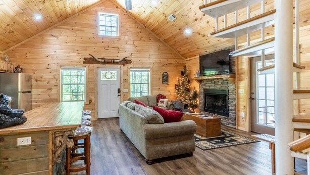 L’intérieur chaleureux d’un chalet en rondins, avec un plafond en bois, une cheminée en pierre, un canapé et un coin repas doté d’un bar.