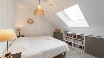 A bedroom with a skylight, a bed, a bedside table with a lamp, a bookshelf, and a decorative mirror.