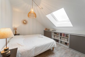 A bedroom with a skylight, a bed, a bedside table with a lamp, a bookshelf, and a decorative mirror.