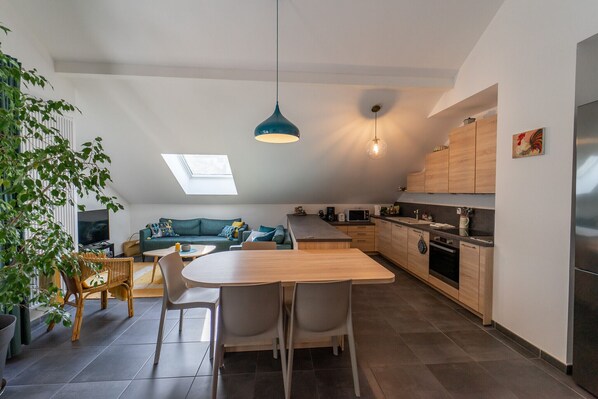 A modern kitchen with a dining area, a sofa, and a TV.