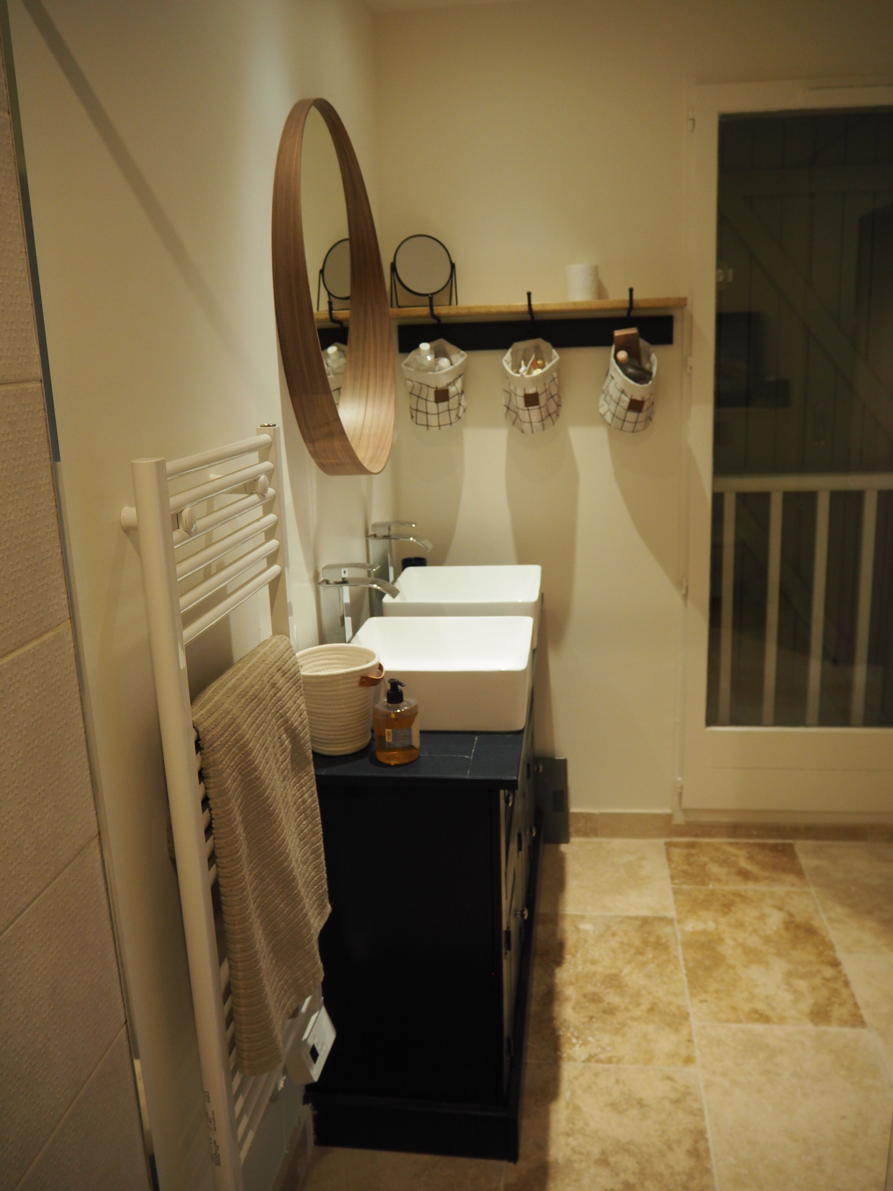 A bathroom with two sinks, a towel rack, a mirror, and a shelf with baskets.