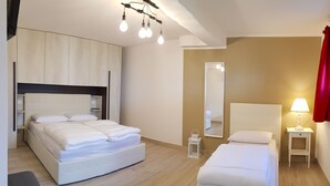 Ein modernes Hotelzimmer mit einem großen Bett, einem kleineren Bett, einem Nachttisch mit Lampe, einem Spiegel und einer Hängeleuchte.