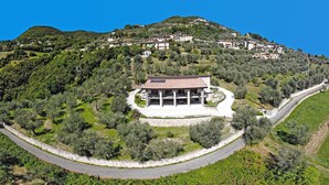 A hillside villa with a curved driveway, surrounded by olive trees and a view of other buildings on the hill. - Villa Vagne Sunset Lake View Patio (Tremosine)